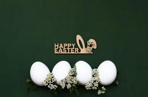 Festive Easter white eggs with white small flowers on a green background. N.. Stock Photos
