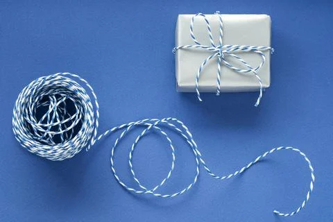 Festive flat lay: gift in silver box and blue gift wrapping rope on blue back Stock Photos