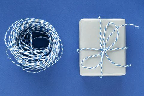 Festive flat lay: gift in silver box and blue gift wrapping rope on blue back Stock Photos