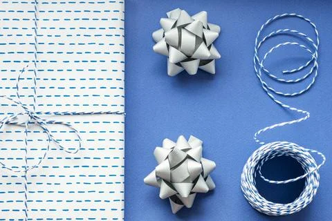 Festive flat lay: gift in white or silver box, blue gift rope, silver bows to Stock Photos