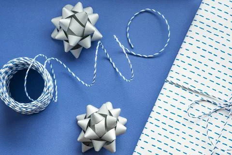 Festive flat lay: gift in white or silver box, blue gift rope, silver bows to Stock Photos