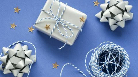 Festive flat lay: gift in white or silver box, blue gift rope, silver bows to Stock Photos