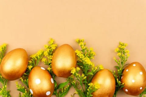 Festive flat lay with golden easter eggs and Solidago flowers on brown back.. Stock Photos