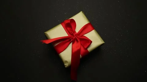 Festive gift in gold packaging and a red bow on a black background. Close-up Stock Footage 156062946