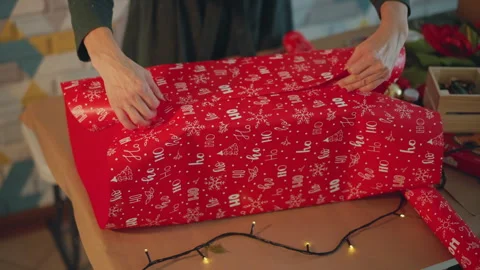 Festive gift wrapping. Artisan wraps presents amidst glowing fairy lights Stock Footage 333306315