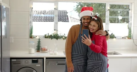 Festive kitchen decor inspiring diverse couple leaning in for smartphone selfie, Stock Footage 344644409