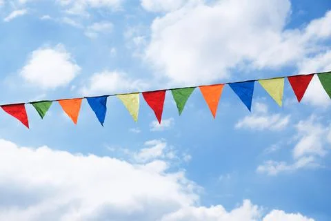 Festive ribbon of multicolored triangle flags on the white clouds and blue sk Stock Photos