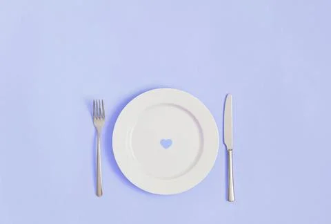 Festive romantic minimal table setting with a heart in a plate on a violet ba Stock Photos