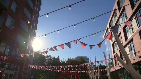 Festive string lights and colorful flags hang above an open urban square in Stock Footage 289452046