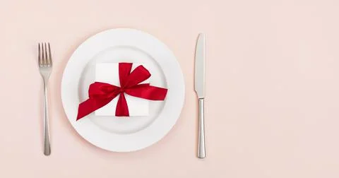 Festive table setting with a gift in a plate on a pink background. Banner. Stock Photos
