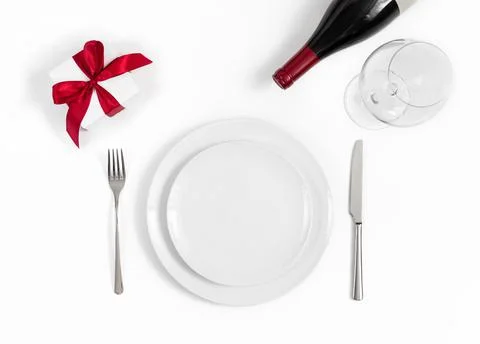 Festive table setting with a gift, wine and dishes on a white background. Stock Photos