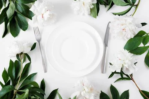 Festive table setting with white plate, cutlery and peonies Stock Photos