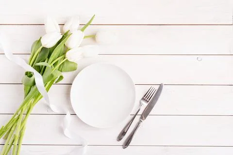 Festive table setting in white, white plate and tulips top view on wooden bac Stock Photos