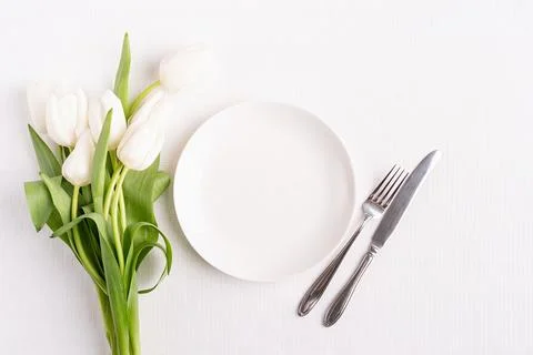 Festive table setting in white, white plate and tulips top view on background Stock Photos