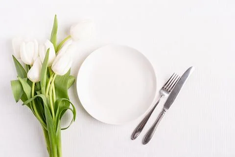 Festive table setting in white, white plate and tulips top view on background Stock Photos