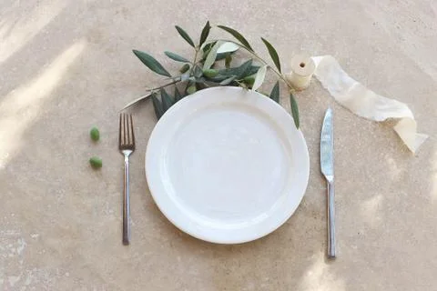 Festive table summer setting with silver cutlery, olive branch, porcelain plate Fotos de archivo