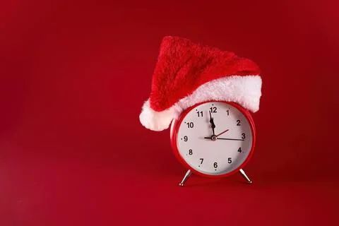 Festive Time. A red clock adorned with a Santa hat against a vibrant red Stock Photos