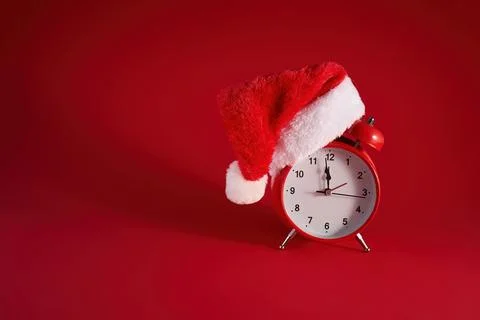 Festive Time. A red clock adorned with a Santa hat against a vibrant red Stock Photos