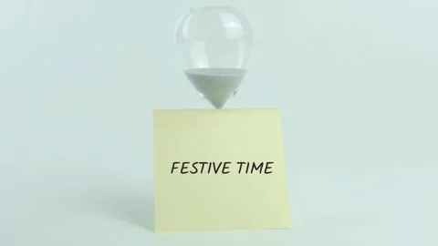 Festive time written on yellow sticky note placed on hourglass on white Stock Footage 313482933