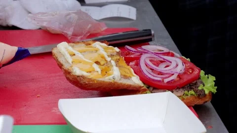 Festive vendor assembles burger, Culinary artist constructs layered snack at Stock Footage 324646065