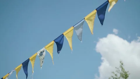 Festive yellow and blue triangular flags on cord moving in wind against blue sky Stock Footage 226906674