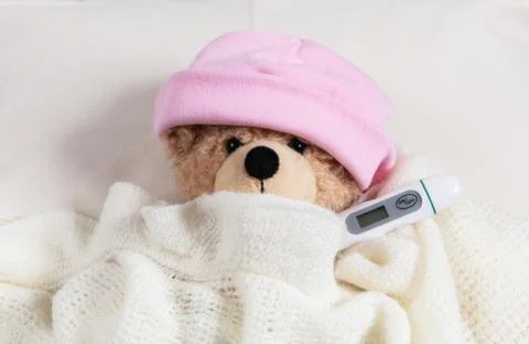 Fever, cold, flue concept. Cute teddy girl with a thermometer in bed, covered Foto stock