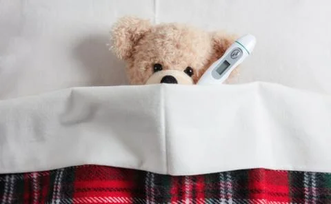 Fever, cold, flue concept. Cute teddy with a thermometer in bed, covered with Stock Photos