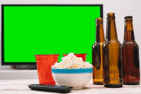 A few bottles of beer with popcorn on a table in front of a green screen TV Stock Photos