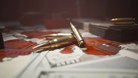 Few bullets lying on the table filled with dollar bills stained with blood. 4KHD Video stock 112602299