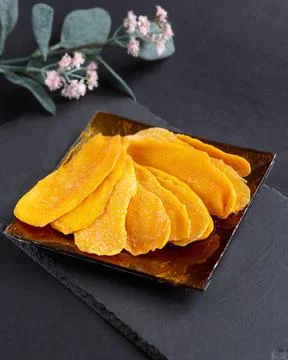 A few pieces of dried mango on a square glass plate on a black background Stock Photos