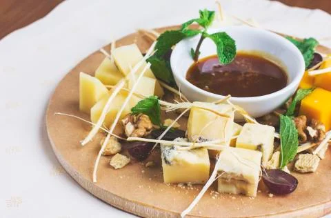 A few types of cheese sliced on a round wooden board with grapes, honey Stock Photos