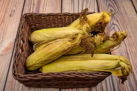 A few untreated ears of corn in a wicker basket on a wooden background. Autum Stock Photos