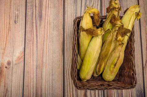 A few untreated ears of corn in a wicker basket on a wooden background. Autum Stock Photos