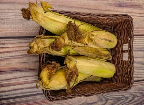 A few untreated ears of corn in a wicker basket on a wooden background. Autum Stock Photos