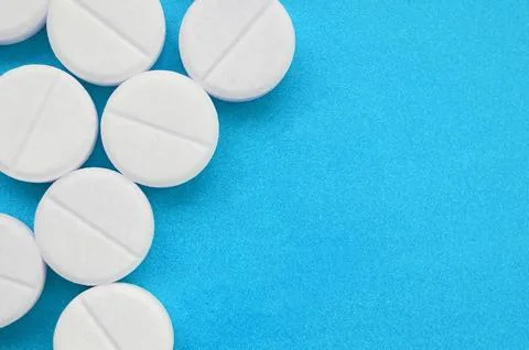 A few white tablets lie on a bright blue background surface. Background ima.. Stock Photos