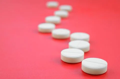 A few white tablets lie on a bright red background surface. Background imag.. Stock Photos