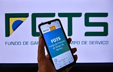 The FGTS logo, on the screen of a cell phone being held by a hand Stock Photos