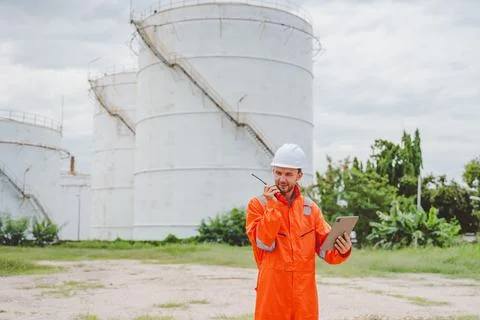 Field engineer using tablet and radio to coordinate inspection at oil stora.. Stock Photos