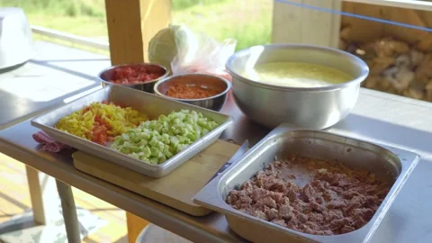 In field kitchen, vegetables and meat are laid out on table in aluminum bowls Stock Footage 153153372