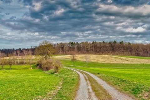 A field path in the middle of a landscape with meadows and fields, in the bac Stock Photos