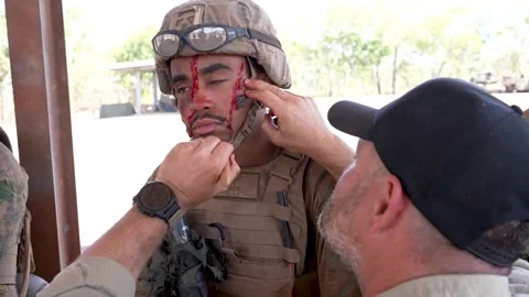 Field simulation technician applying fake blood to soldiers face Stock Footage 280470125