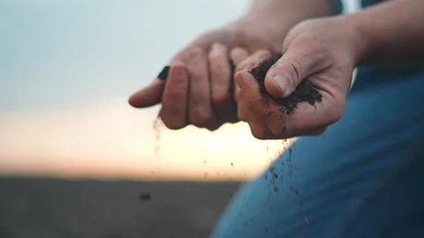 Field at sunset as hands release fine dirt. Earth texture slips slowly Stock Footage 319249482