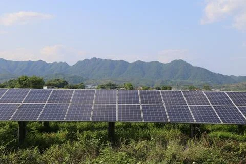 In the field, there is an array of solar panels with mountains in the backg.. Stock Photos