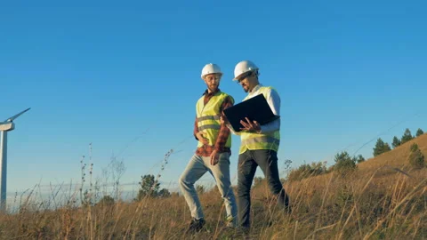 A field with two energetics experts walking across it and a functioning turbine Video stock 97987288