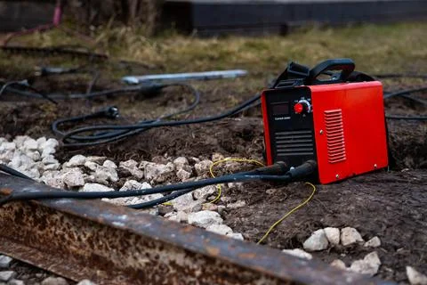 Field welding setup with red arc welder, cables, and steel beams Fotos Stock