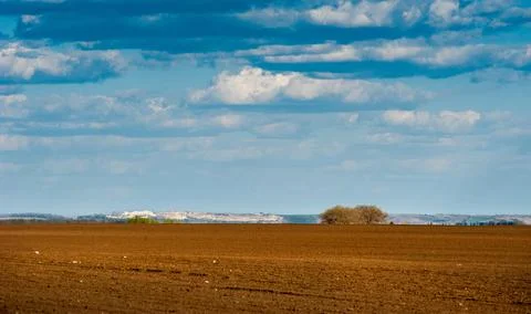Fields prepared for sowing, smooth lines on hilly terrain with a cloudy sky Stock Photos