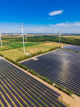 Fields with solar panels and wind turbines during clear weather Stock Photos