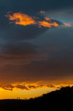 Fiery evening sky with orange clouds and hillside silhouette Stock Photos