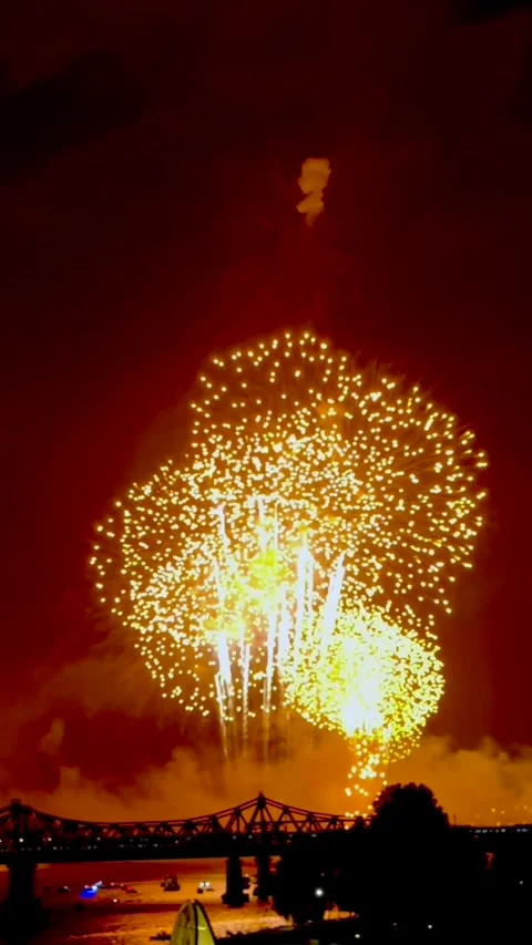 Fiery explosion of light fills night sky, reflecting over river as golden Stock Footage 324687738