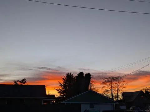 Fiery orange and red sunset clouds stretch above a green house Stockfoto's